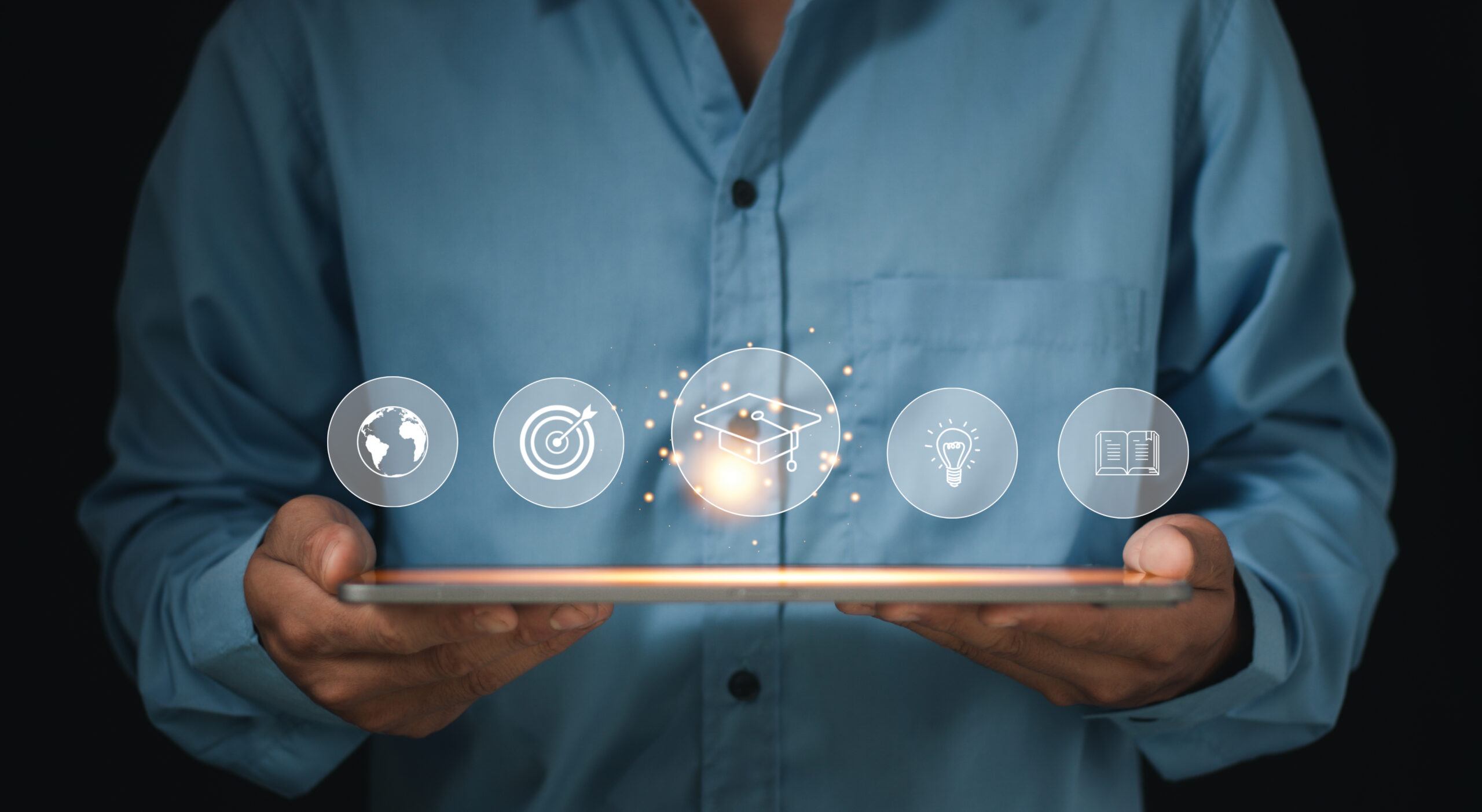 hands holding a laptop with icons floating above highlighting an education icon.